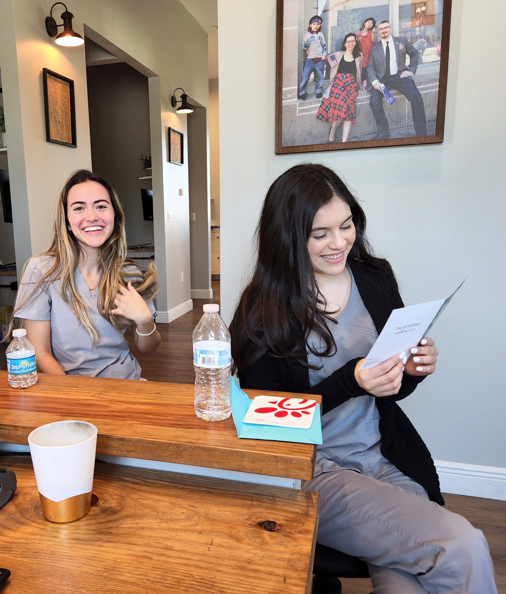 Two women in scrubs smiling at a table.